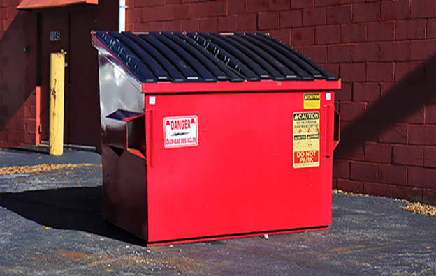 Green front-load dumpster positioned in a paved service area behind a business.